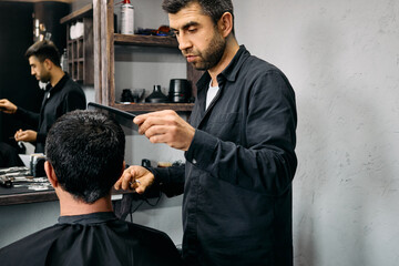 A skilled barber carefully styles the hair of a client seated in a barber chair. The modern salon is well-equipped with tools and has a sleek, contemporary design