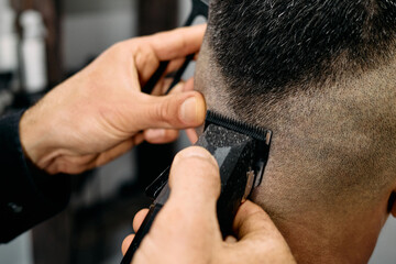 A skilled barber is using clippers on a client's hair, focusing on a clean fade. The interior...