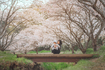 Happy asian toddler baby girl in cute bear outfit playing with mother on wooden bridge surrounded...