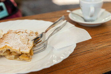 tazzina con caffè espresso, al bar, su un tavolo di legno, accompagnata con un piatto di strudel con due forchette