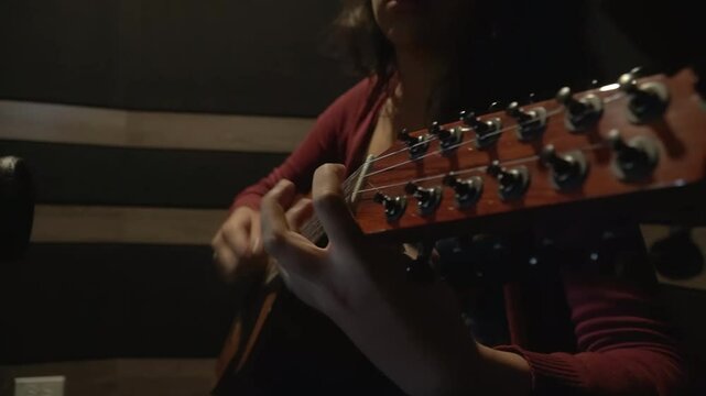 Close-up of woman's hands playing colombian Tiple in a studio setting. The focus is on the musician and her instrument, highlighting the intimate and focused nature of a studio session. 