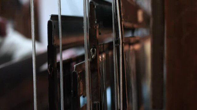 Extreme close-up video detailing the inner workings of a traditional handloom, specifically focusing on the metallic heddles. 