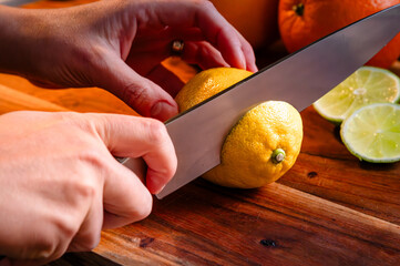 Person slicing into a whole lemon on a wood cutting board with a lime in the background