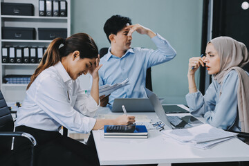 Young asian businesswoman suffering from headache while colleagues arguing and blaming her for bad...