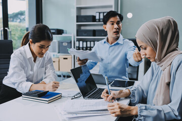Young asian businesswoman suffering from headache while colleagues arguing and blaming her for bad work results during stressful office meeting