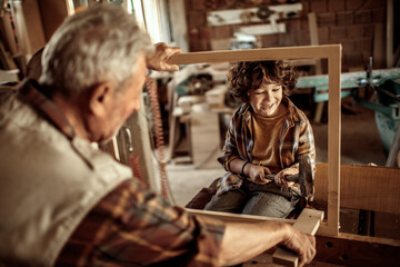 Grandfather teaching grandson woodworking in home workshop
