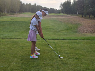 Coach and teenage child play golf on sunny day on a lush green course