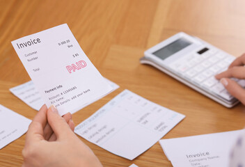 Fototapeta premium Paying bills. Woman with different invoices and calculator at wooden table indoors, closeup