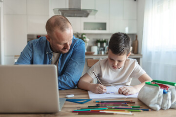 Fototapeta premium Father and son sitting side by side at home to work and study. Caucasian ethnicity father and son working and learning at home during the day.