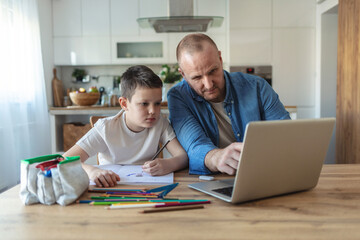 Fototapeta premium Father and son sitting side by side at home to work and study. Caucasian ethnicity father and son working and learning at home during the day.