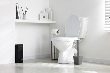 Toilet, brush and necessities near white wall in bathroom