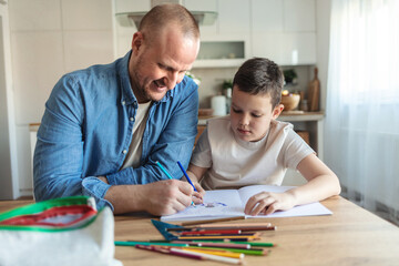 Caucasian boy doing homework with his dad. A handsome young man helping his son with school work at...