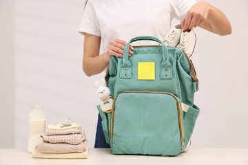 Mother packing baby's stuff into bag at white table, closeup