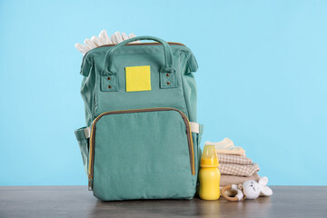 Mother's bag with baby's stuff on wooden table against light blue background