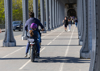 Un papa et sa fille en train de faire du vélo à Paris, sous le pont de bir hakeim, sur une piste cyclable. Le format de l'image est horizontal.