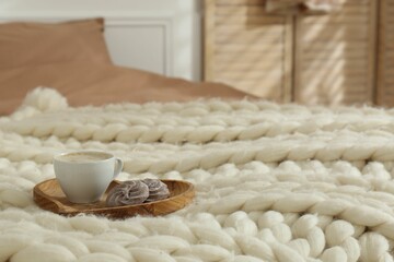 Cup of coffee with cookies on knitted merino wool plaid in bedroom, space for text