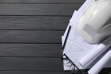 Different engineering drawings, hard hat, glasses and pencil on grey wooden table, flat lay. Space for text
