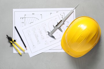 Different engineering drawings, hard hat, pencil, divider and vernier caliper on grey table, flat...