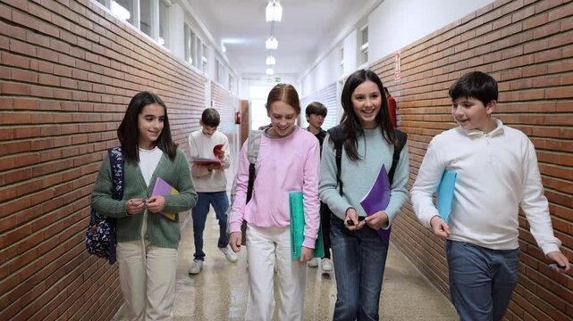 Cheerful group of school students walking and conversing together in bright hallway during break, sharing animated conversation and friendship between classes