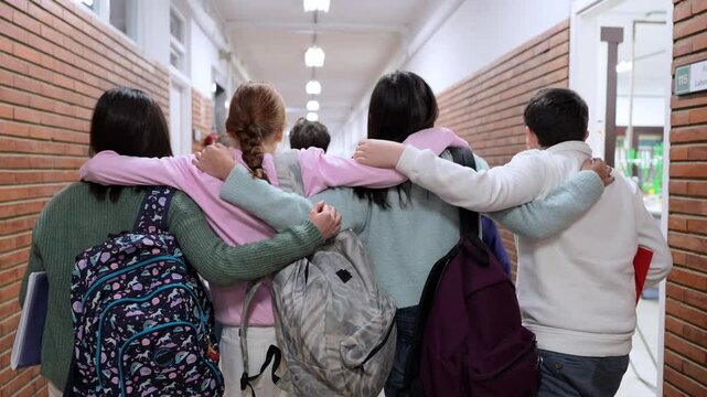 Four students walk down school hallway with arms around each other, demonstrating camaraderie and unity