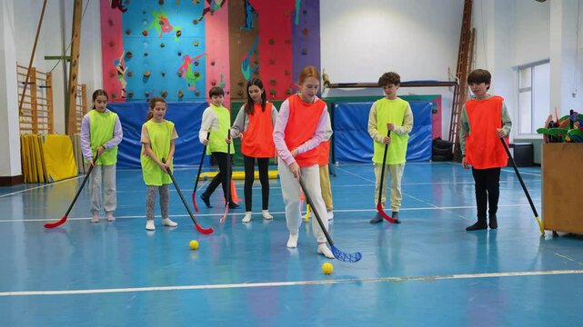 Young students in colorful vests practicing floorball together, learning teamwork and enjoying physical education in school gymnasium with energetic movement and enthusiasm