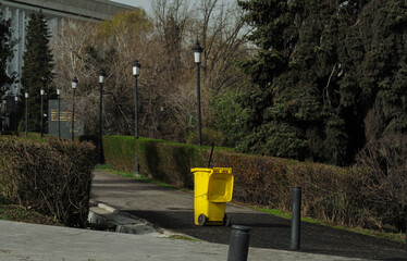 A yellow trash can on wheels stands on an alley in the city