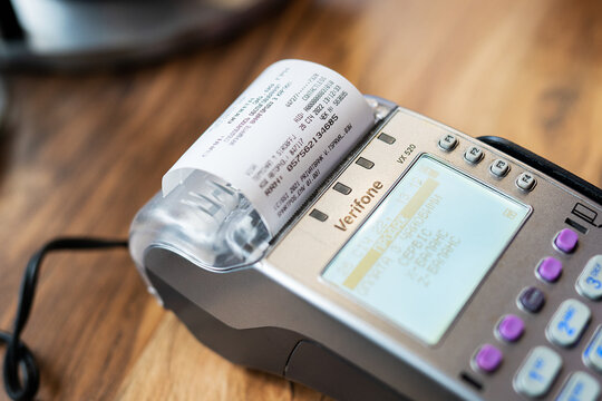 Close-up of a POS payment terminal Verifone VX 520 printing a receipt after a contactless transaction. Focus on the machine, receipt paper, screen, and keypad. Kyiv, Ukraine - January 26 2022