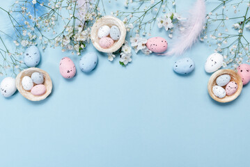 Flat lay of Easter eggs, decorative nests, and blue feathers on pastel blue background, greeting card concept with festive spring design