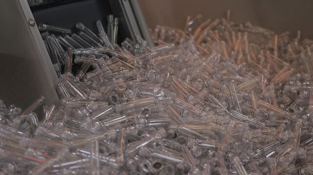 Clear plastic preforms are being poured into a pile from a machine. This industrial setting highlights the mass production of plastic packaging.