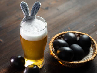 A glass of beer with bunny ears for the Easter holiday, Easter eggs painted dark. Wooden table