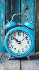 Blue alarm clock sits, telling time on weathered wooden surface, against turquoise painted wood wall