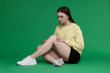 Young woman suffering from pain in knee on green background