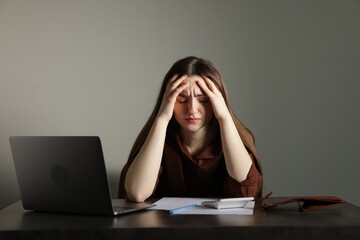 Upset woman at grey table with laptop, calculator and wallet. Financial problems