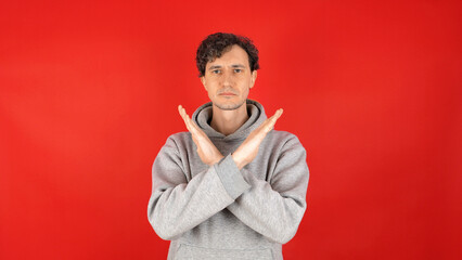 young adult curly serious man raises hands, crosses arms, showing in front sign stop, ban, rejected...