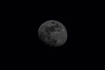 A zoomed in shot of the moon during a dark night, it is not quite full.