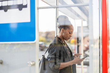 Woman using her mobile phone at a bus stop in the city

