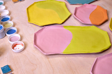 top view of handmade clay plates covered with colored glazes and glaze jars, ready for firing