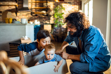 Father playing with kids while unpacking moving boxes at home
