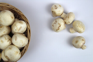 There is a basket of mushrooms on a white background, and a few more are lying in a pile nearby.