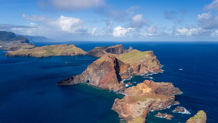 Coastal cliffs rise dramatically from crystal-clear waters at a remote island location under a vibrant blue sky