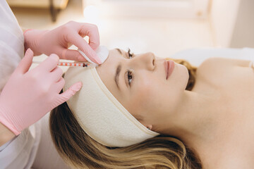 Cosmetologist making rejuvenating injection for young woman lying on couch in beauty salon