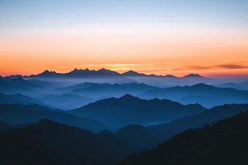 Fototapeta premium Layered mountain ranges shrouded in mist under a vibrant orange and blue gradient sky at dawn or dusk