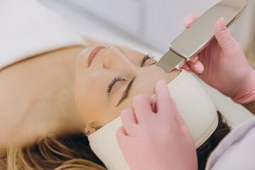 Close up of a cosmetologist using an ultrasonic scrubber during a facial treatment, promoting...