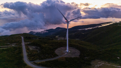 Radiant sunset over a solitary wind turbine amidst rolling hills and distant clouds