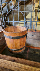 An antique wooden bucket with metal hoops is suspended over a wooden well. Natural materials, vintage style, historical surroundings.