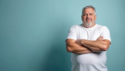 Portrait of overweight man with crossed arms wearing white t-shirt. Mature male poses confidently. Serious face expression. Concept of body positivity. Blue background with copy space.