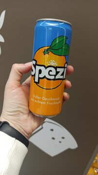 A hand holding a colorful Spezi soda can with orange fruit design against a plain background in Vienna, Austria, 26 March 2025