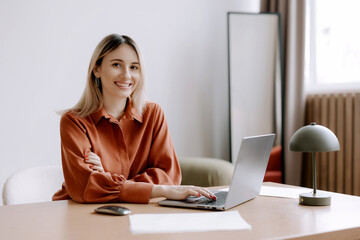 Young professional woman working at a desk with a laptop in a modern office setting during daylight...