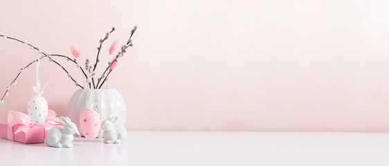 Festive decor on an Easter theme with a cute bunny and hanging Easter eggs on willow branches against a beige wall. Happy Easter. Banner