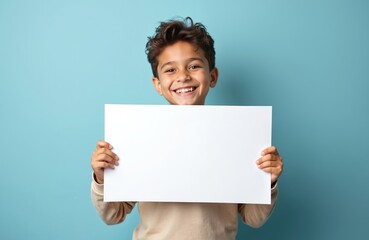 Handsome boy holding blank white placard poster against pastel blue background. Happy kid shows mock up sign. Child holding empty paper with copy space for text design. Perfect for advertising sales